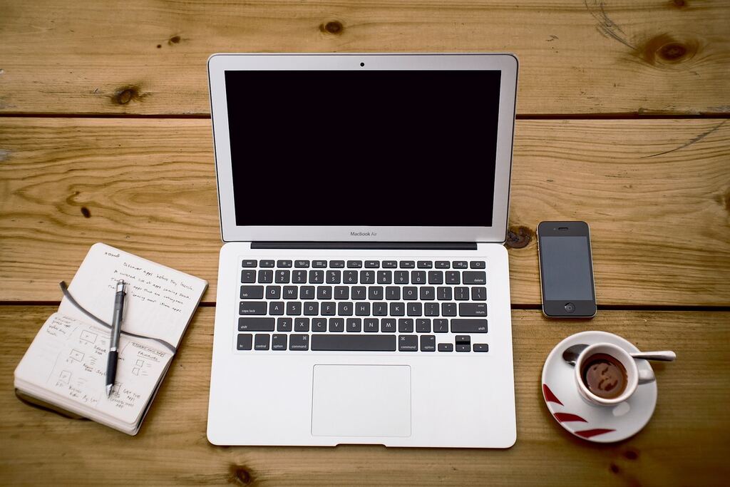 Laptop, Notizbuch, Smartphone und Kaffeetasse auf einem Holztisch