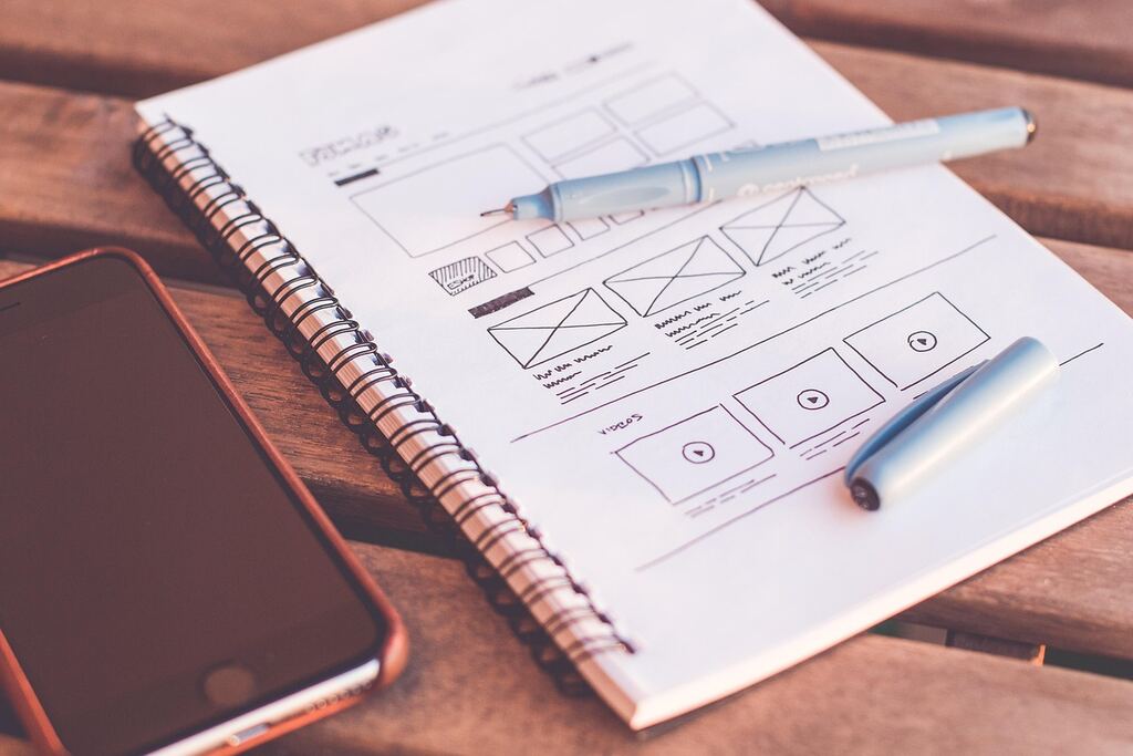 Notizbuch mit skizziertem Seitenlayout, daneben Stifte und ein Smartphone